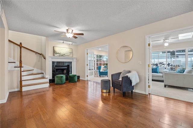 living room featuring hardwood / wood-style flooring, a textured ceiling, a fireplace, and ceiling fan