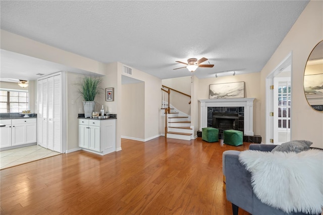 living room featuring ceiling fan, light hardwood / wood-style floors, a tile fireplace, and a textured ceiling