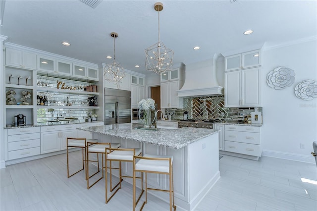 kitchen with open shelves, custom range hood, white cabinets, an island with sink, and stainless steel built in refrigerator