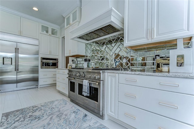 kitchen with light stone counters, custom range hood, decorative backsplash, and high quality appliances