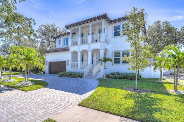 mediterranean / spanish home with a balcony, a garage, decorative driveway, stucco siding, and a front yard