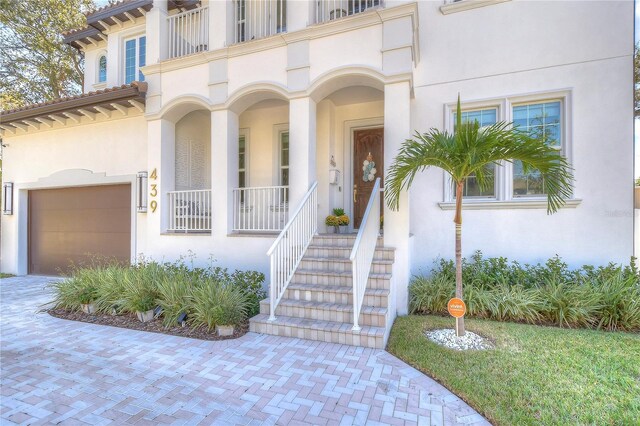 entrance to property with a garage, covered porch, and stucco siding