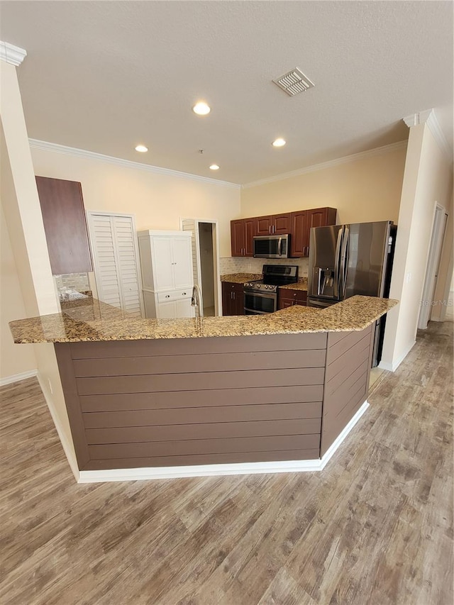 kitchen featuring ornamental molding, appliances with stainless steel finishes, light hardwood / wood-style floors, and kitchen peninsula