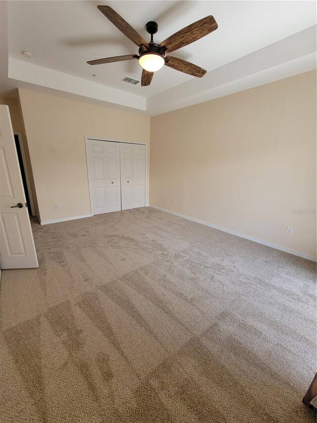 unfurnished bedroom featuring a closet, a raised ceiling, ceiling fan, and carpet