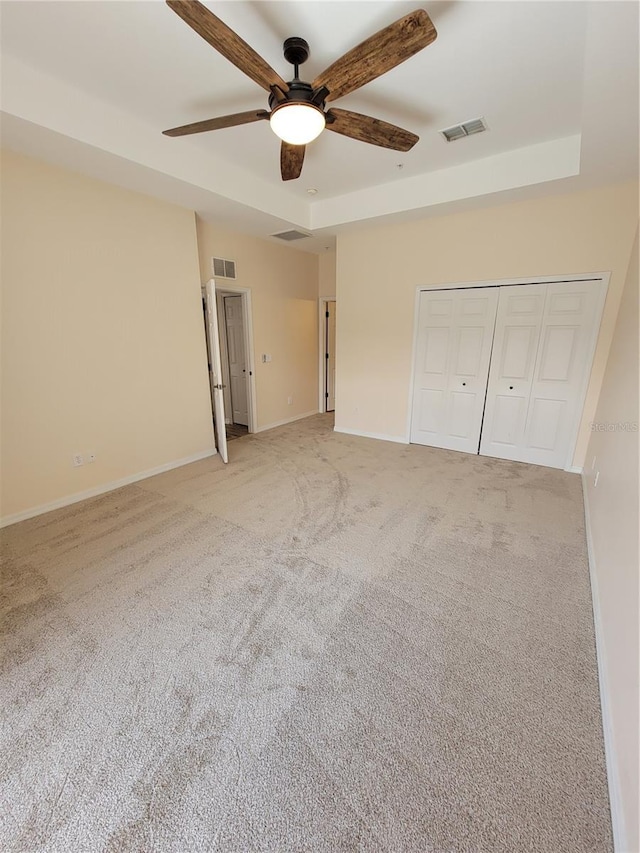 unfurnished bedroom featuring a raised ceiling, light carpet, ceiling fan, and a closet