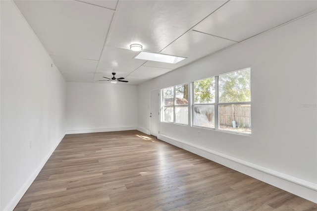 unfurnished room featuring ceiling fan, a skylight, and light hardwood / wood-style flooring