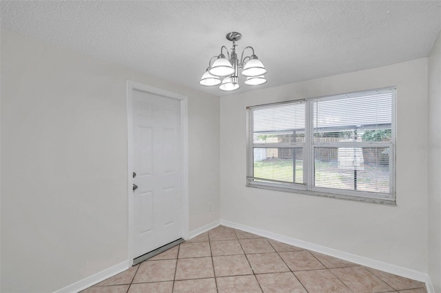 spare room with a textured ceiling, a chandelier, and light tile patterned flooring