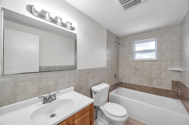 full bathroom with tiled shower / bath, tile walls, tile patterned flooring, vanity, and toilet