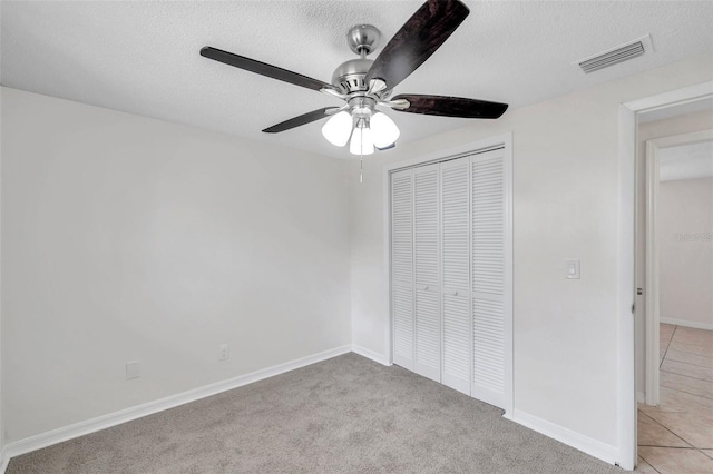 unfurnished bedroom with ceiling fan, light colored carpet, a closet, and a textured ceiling