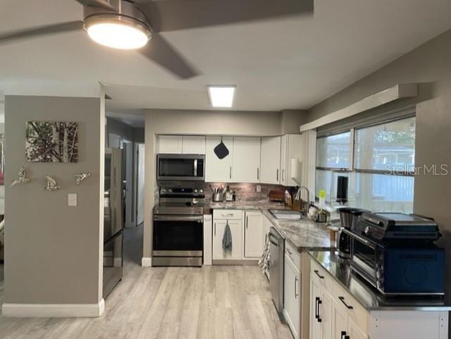 kitchen featuring tasteful backsplash, white cabinetry, sink, stainless steel appliances, and light hardwood / wood-style flooring