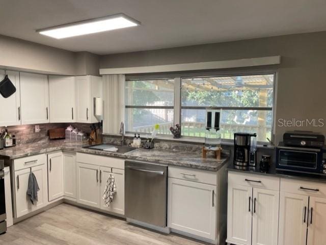 kitchen with white cabinetry, sink, dark stone counters, stainless steel appliances, and light hardwood / wood-style flooring