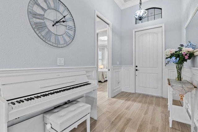 foyer entrance featuring a chandelier, light wood finished floors, wainscoting, and ornamental molding