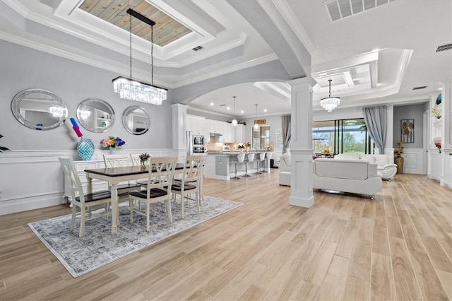 dining area featuring a tray ceiling, light wood-style flooring, and ornate columns