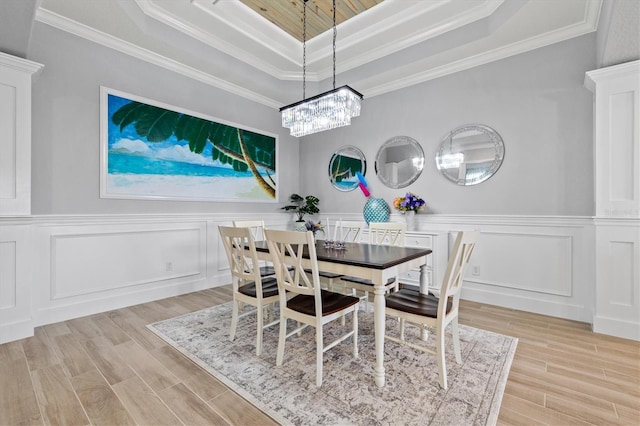 dining space with light wood-type flooring, a tray ceiling, a decorative wall, and crown molding