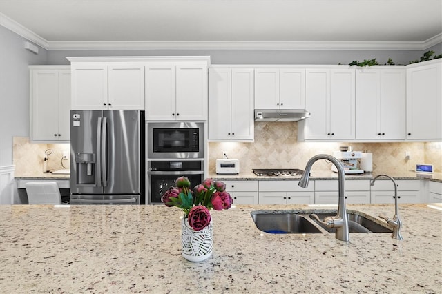 kitchen with white cabinets, appliances with stainless steel finishes, ornamental molding, under cabinet range hood, and a sink