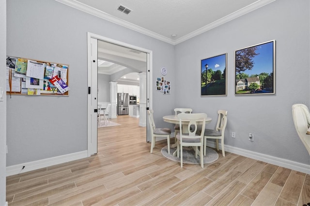 dining space with light wood finished floors, visible vents, arched walkways, baseboards, and ornamental molding