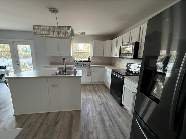 kitchen featuring white cabinetry, stainless steel appliances, decorative light fixtures, and a kitchen island with sink