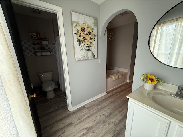 bathroom featuring hardwood / wood-style flooring, a tub to relax in, vanity, and toilet