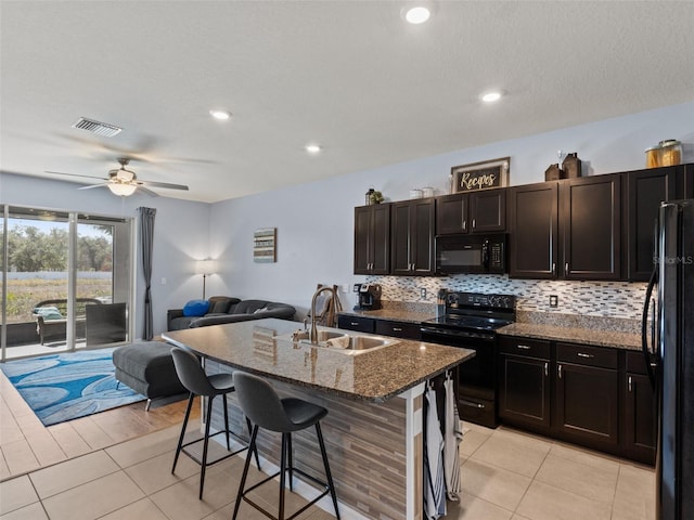 kitchen with sink, dark stone countertops, a kitchen breakfast bar, black appliances, and a center island with sink