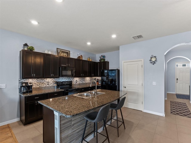 kitchen featuring sink, a breakfast bar area, black appliances, a kitchen island with sink, and backsplash