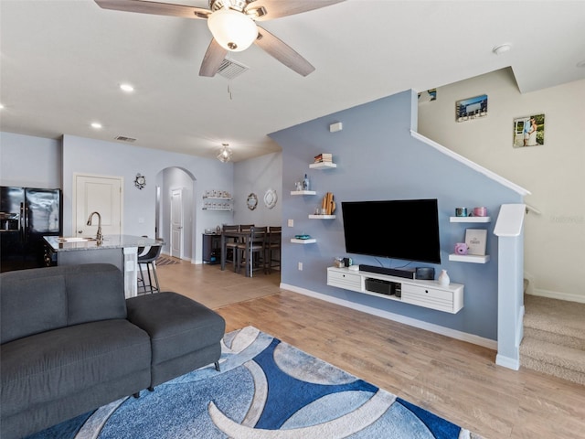 living area featuring baseboards, arched walkways, light wood-style floors, and ceiling fan