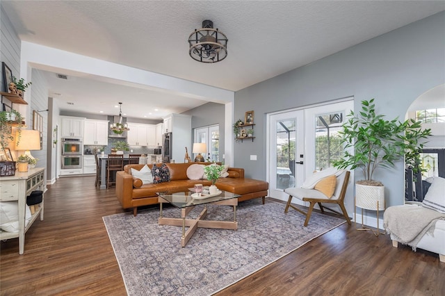 living room featuring french doors, dark hardwood / wood-style floors, an inviting chandelier, and a textured ceiling