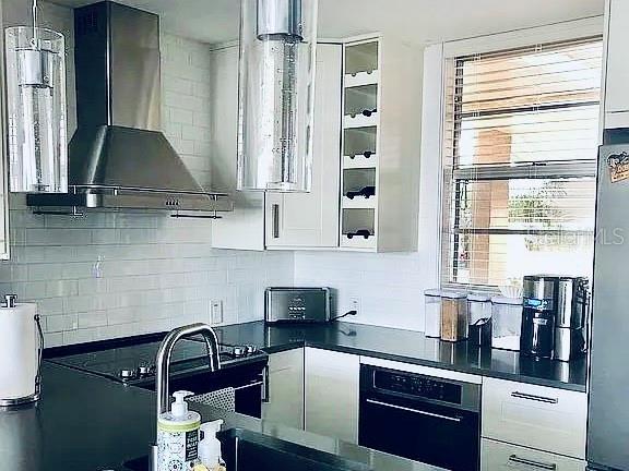 kitchen with wall chimney range hood, backsplash, stainless steel fridge, and white cabinets