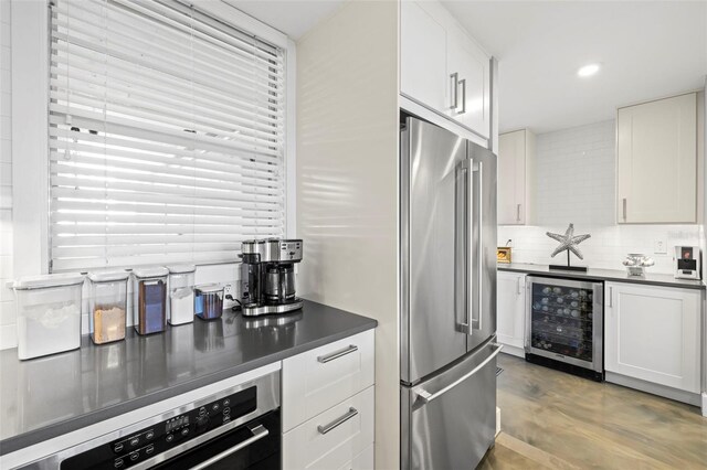 kitchen featuring high end fridge, beverage cooler, backsplash, dark countertops, and white cabinetry