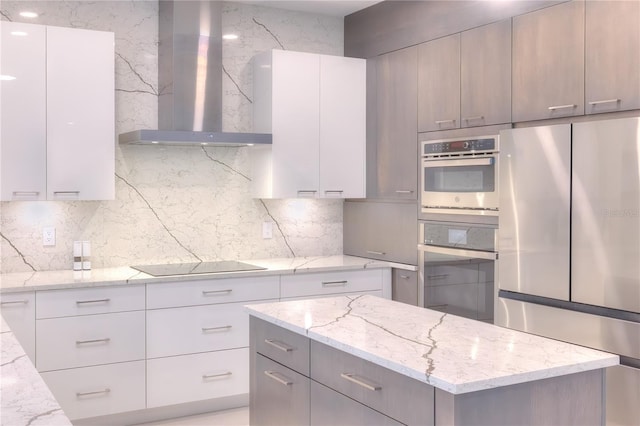 kitchen with light stone counters, gray cabinetry, appliances with stainless steel finishes, and wall chimney range hood