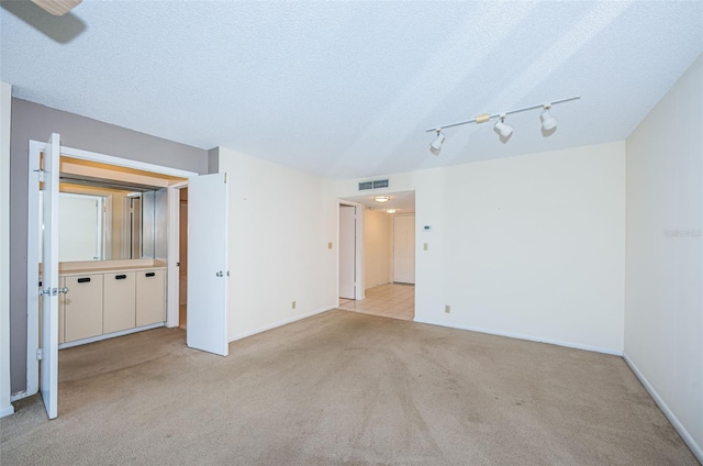 carpeted empty room featuring rail lighting and a textured ceiling