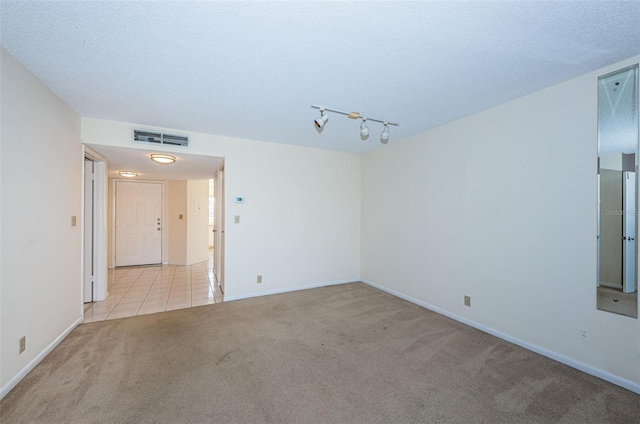 spare room featuring rail lighting, light carpet, and a textured ceiling