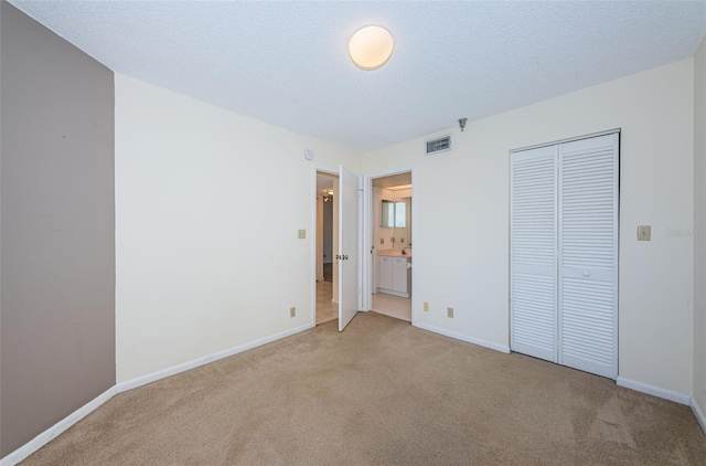 unfurnished bedroom featuring connected bathroom, light colored carpet, a closet, and a textured ceiling