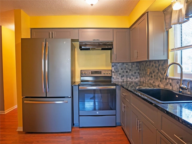 kitchen with sink, dark stone countertops, appliances with stainless steel finishes, dark hardwood / wood-style floors, and backsplash