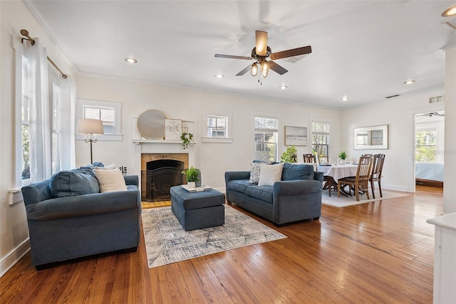 living room with ornamental molding, wood-type flooring, a brick fireplace, and a wealth of natural light