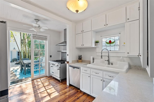 kitchen featuring wall chimney range hood, sink, dark wood-type flooring, appliances with stainless steel finishes, and white cabinetry