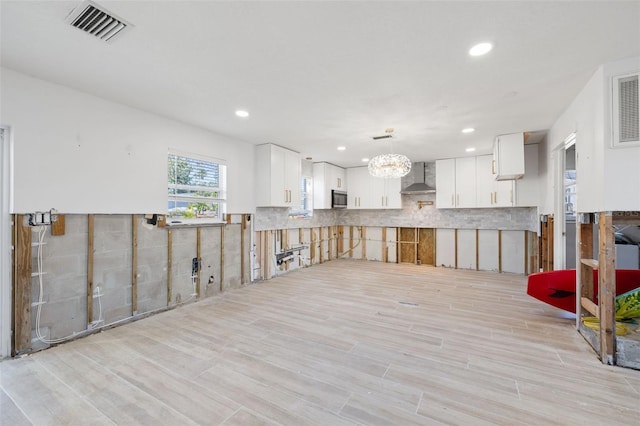 kitchen with wall chimney exhaust hood, white cabinetry, hanging light fixtures, light wood-type flooring, and backsplash