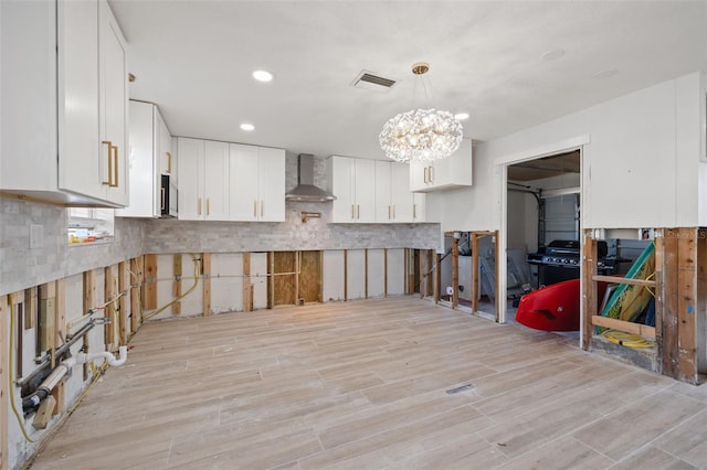 kitchen with white cabinets, decorative backsplash, hanging light fixtures, wall chimney range hood, and light wood-type flooring