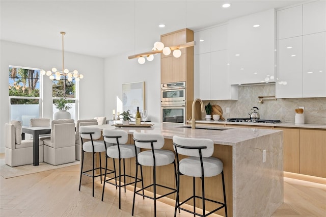 kitchen with appliances with stainless steel finishes, decorative light fixtures, a kitchen island with sink, and white cabinets