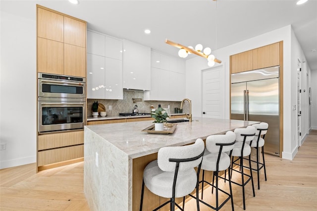 kitchen featuring appliances with stainless steel finishes, pendant lighting, tasteful backsplash, white cabinets, and a center island with sink