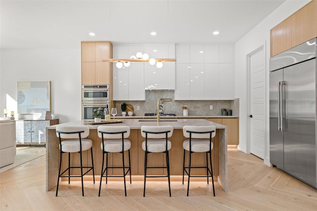 kitchen with a breakfast bar area, white cabinetry, a kitchen island with sink, stainless steel appliances, and decorative backsplash