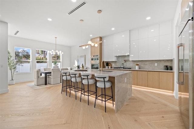 kitchen featuring pendant lighting, sink, light parquet floors, white cabinetry, and a kitchen island with sink