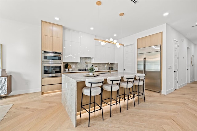 kitchen featuring an island with sink, sink, white cabinets, stainless steel appliances, and light parquet flooring