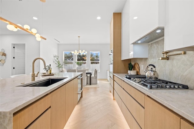 kitchen featuring sink, hanging light fixtures, stainless steel gas stovetop, light stone countertops, and white cabinets