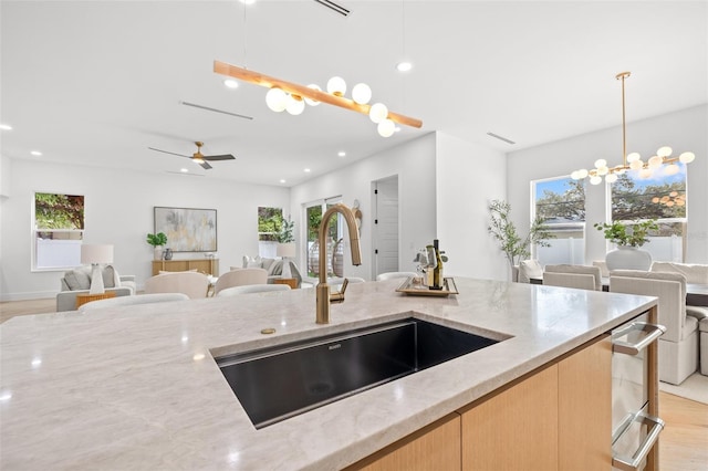 kitchen featuring light brown cabinetry, sink, decorative light fixtures, plenty of natural light, and light stone countertops