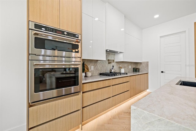 kitchen featuring appliances with stainless steel finishes, white cabinets, decorative backsplash, light parquet floors, and light stone counters