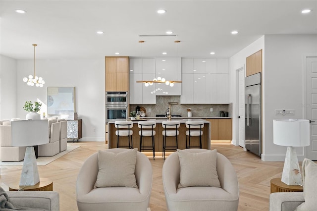 kitchen with pendant lighting, white cabinetry, a kitchen island with sink, stainless steel appliances, and light brown cabinets