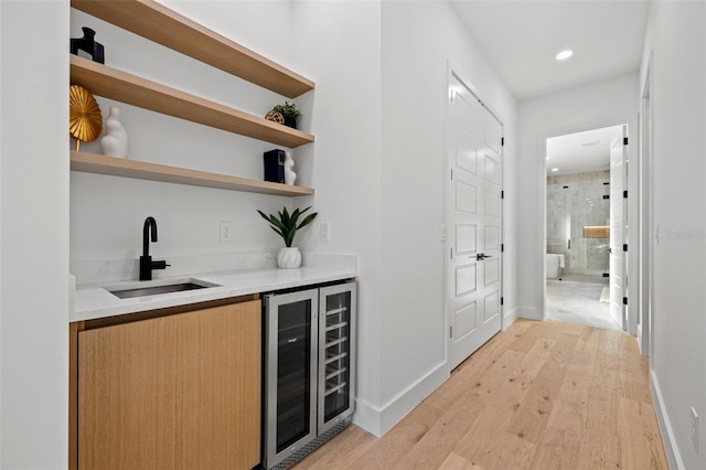 bar with sink, beverage cooler, and light wood-type flooring