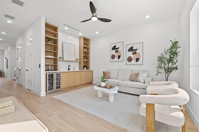 living room with wine cooler, built in shelves, light hardwood / wood-style flooring, wet bar, and ceiling fan