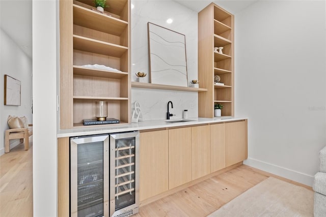 bar with light brown cabinetry, sink, beverage cooler, and light wood-type flooring