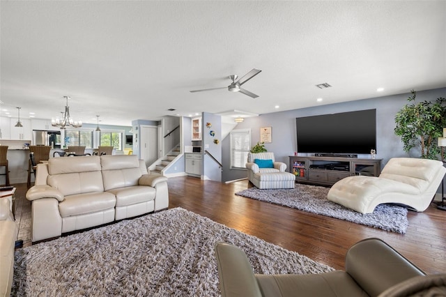 living room featuring dark wood-type flooring, ceiling fan with notable chandelier, and a textured ceiling